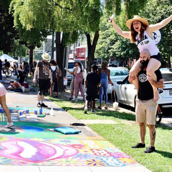 a woman in a chalk it up shirt on the shoulders of a man with a beard as they walk around the chalk it up festival